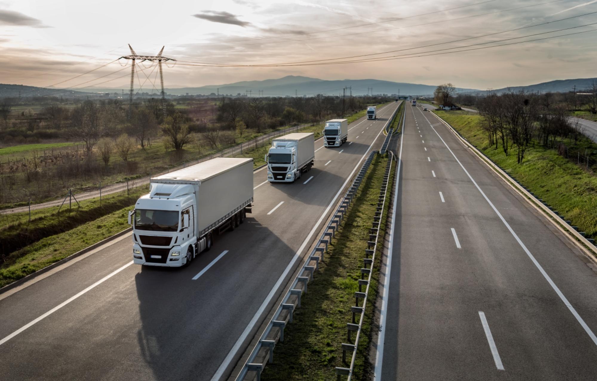 Convoi de camions blancs circulant sur une autoroute au coucher du soleil.